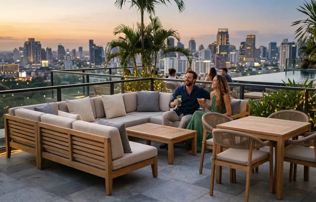 Luxury rooftop lounge with teak outdoor furniture, sectional sofa and dining set overlooking city skyline at sunset.