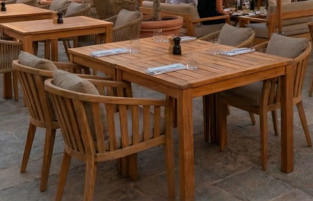 Weather-resistant furniture teak dining table set with cushioned chairs on an outdoor restaurant patio.