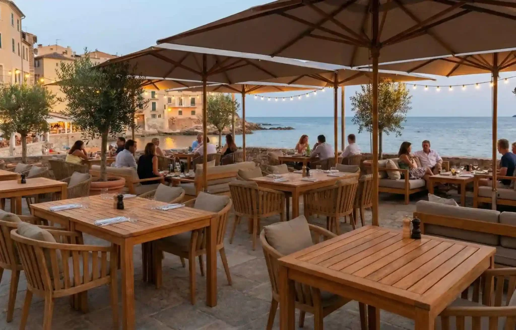 Open-air restaurant terrace with weather-resistant furniture, teak tables, umbrellas, and seaside dining area.